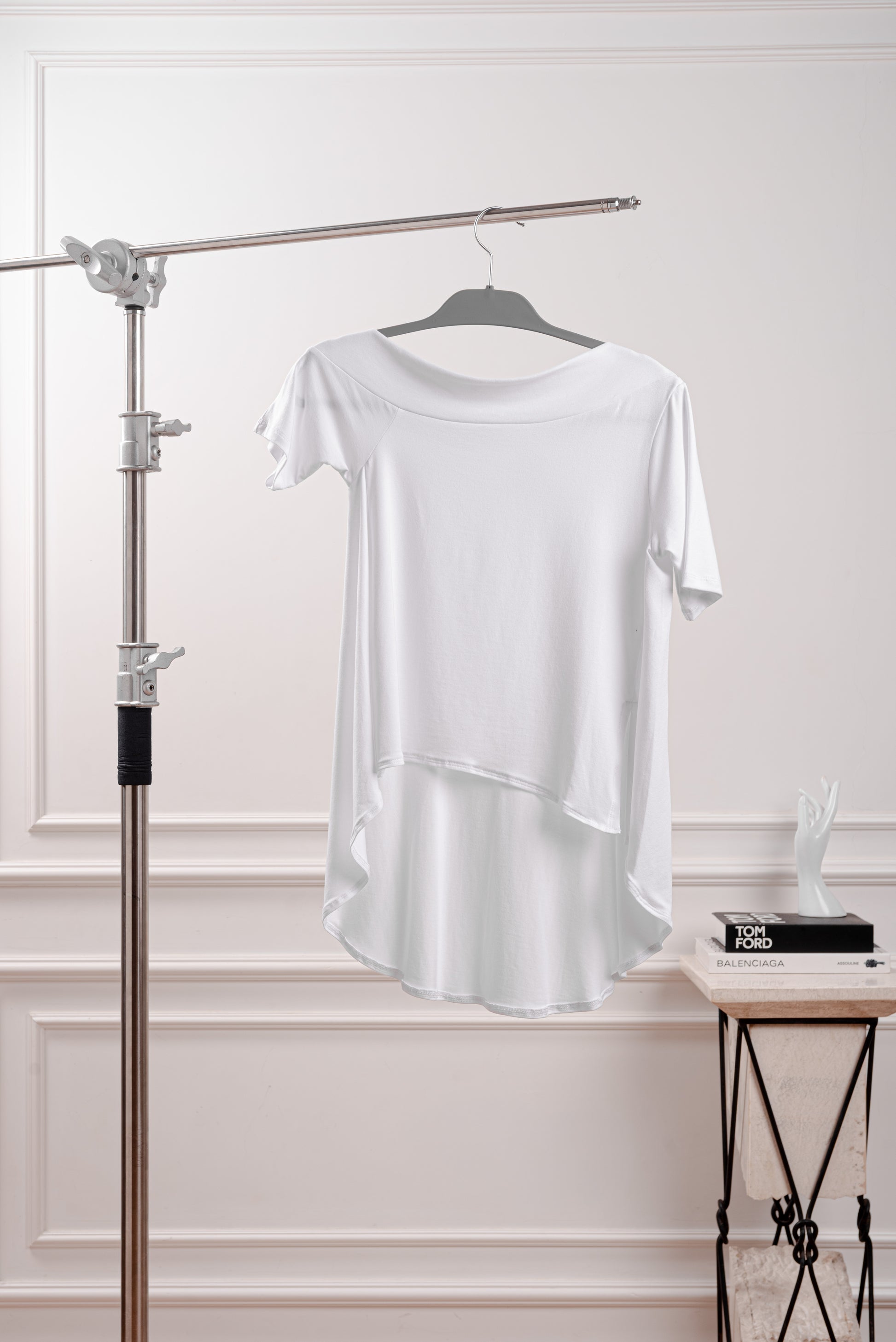 Polo Asimétrico con Cola Larga, color blanco, diseño fluido y deconstruido YouSoul. Detalle del Rib profundo que luce el hombro del Polo Asimétrico con Cola, inspirado en la silueta Rectangular. Vista trasera del polo asimétrico mostrando la caída dramática de la cola larga.