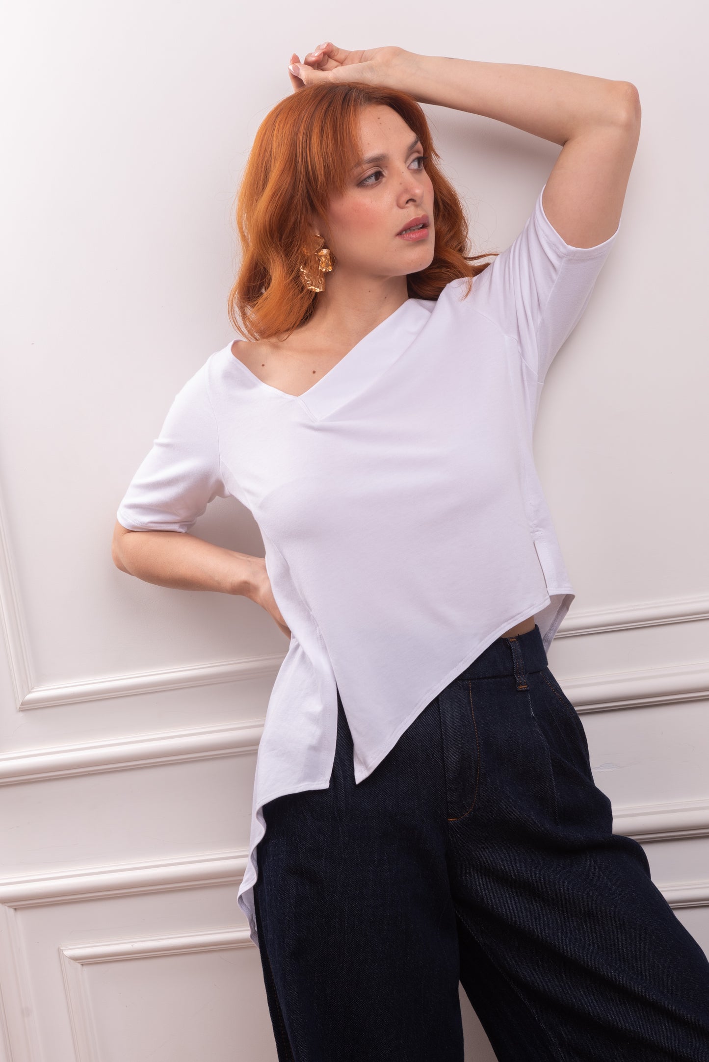 Polo Asimétrico con Cola en Punta, color blanco, con cuello V irregular, ideal para looks de verano. Vista de la cola en punta y fluida del polo asimétrico, diseñado para el dinamismo de la silueta Triángulo Invertido. Primer plano del sofisticado cuello en V irregular del polo de Algodón Pima Modal.