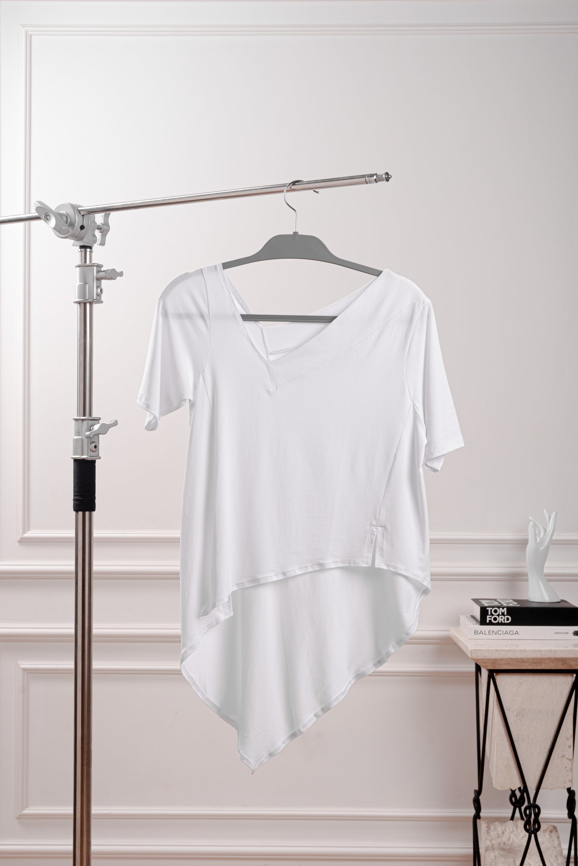 Polo Asimétrico con Cola en Punta, color blanco, con cuello V irregular, ideal para looks de verano.Vista de la cola en punta y fluida del polo asimétrico, diseñado para el dinamismo de la silueta Triángulo Invertido. Primer plano del sofisticado cuello en V irregular del polo de Algodón Pima Modal.