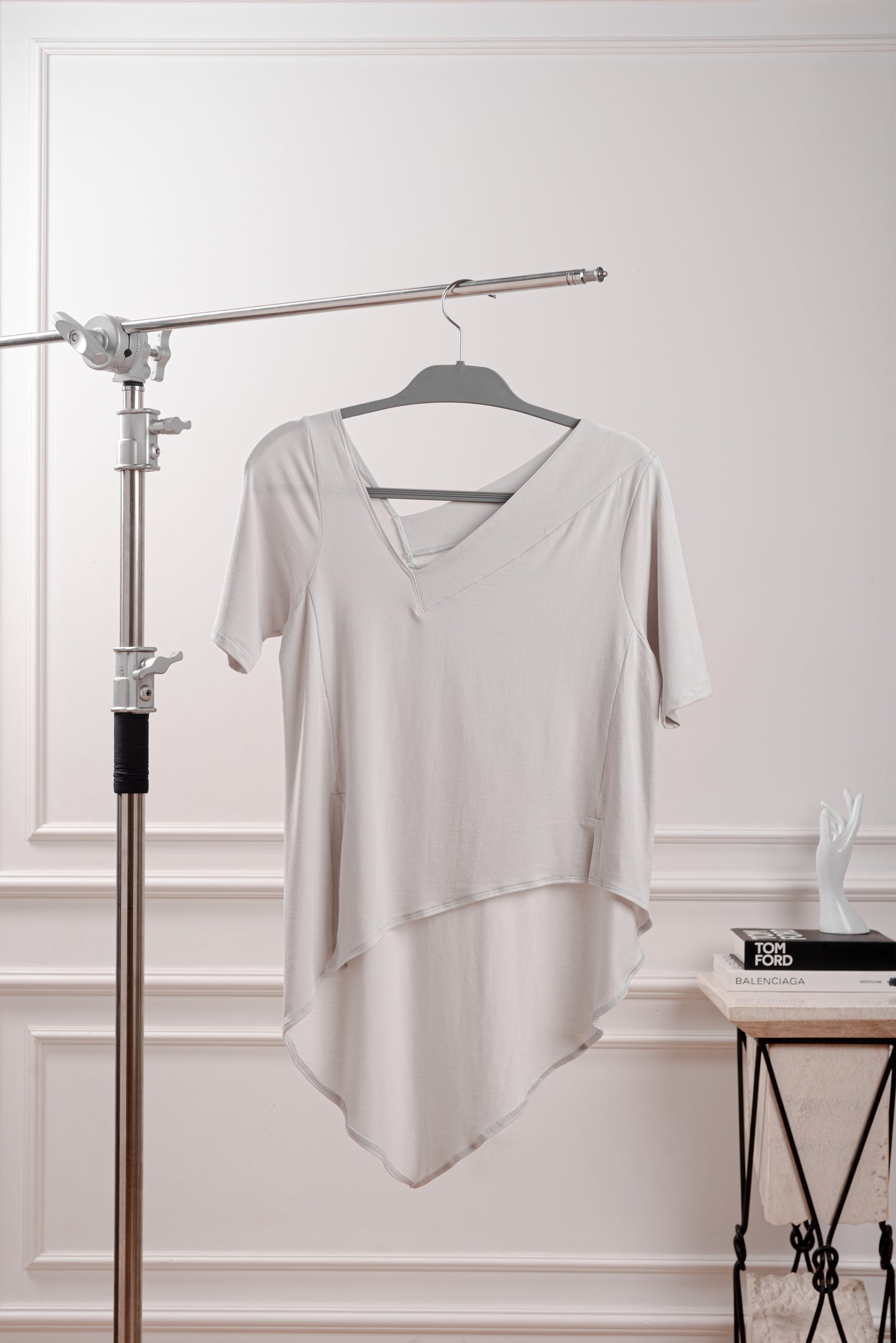 Polo Asimétrico con Cola en Punta, color gris, con cuello V irregular, ideal para looks de verano.Vista de la cola en punta y fluida del polo asimétrico, diseñado para el dinamismo de la silueta Triángulo Invertido. Primer plano del sofisticado cuello en V irregular del polo de Algodón Pima Modal.